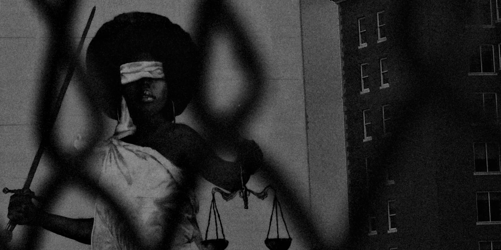 Blindfolded Lady Justice mural in downtown Houston, photographed through a chain-link fence
